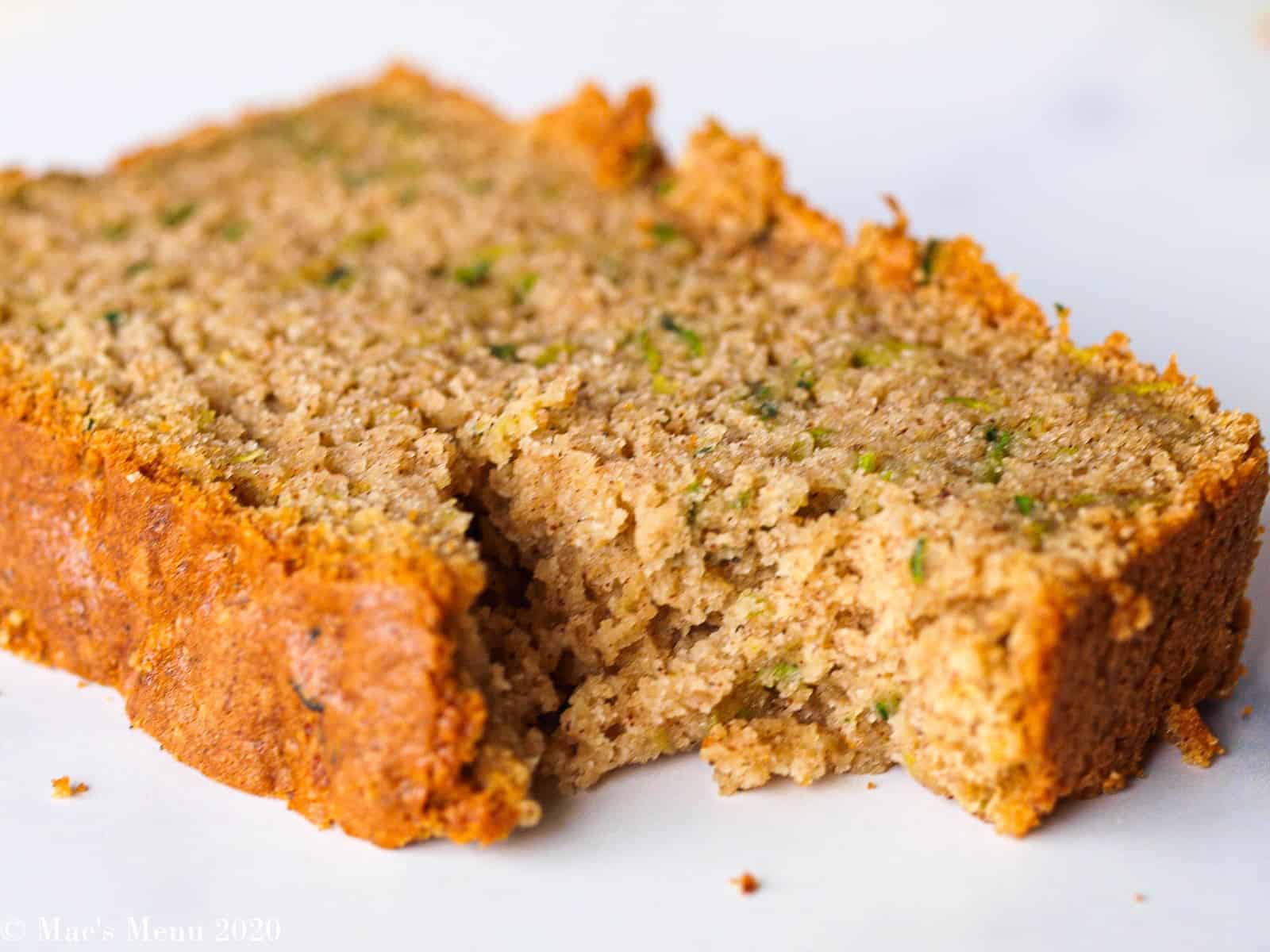 An up-close picture of a piece of gluten-free zucchini bread with a bite taken out of it. 