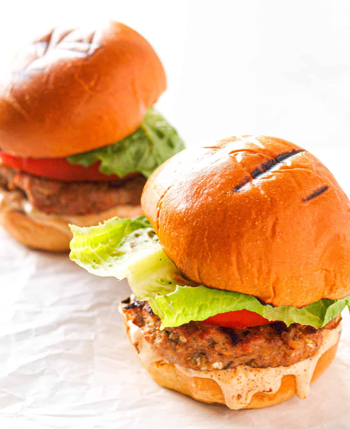 Two jamaican turkey burgers on a piece of white parchment paper