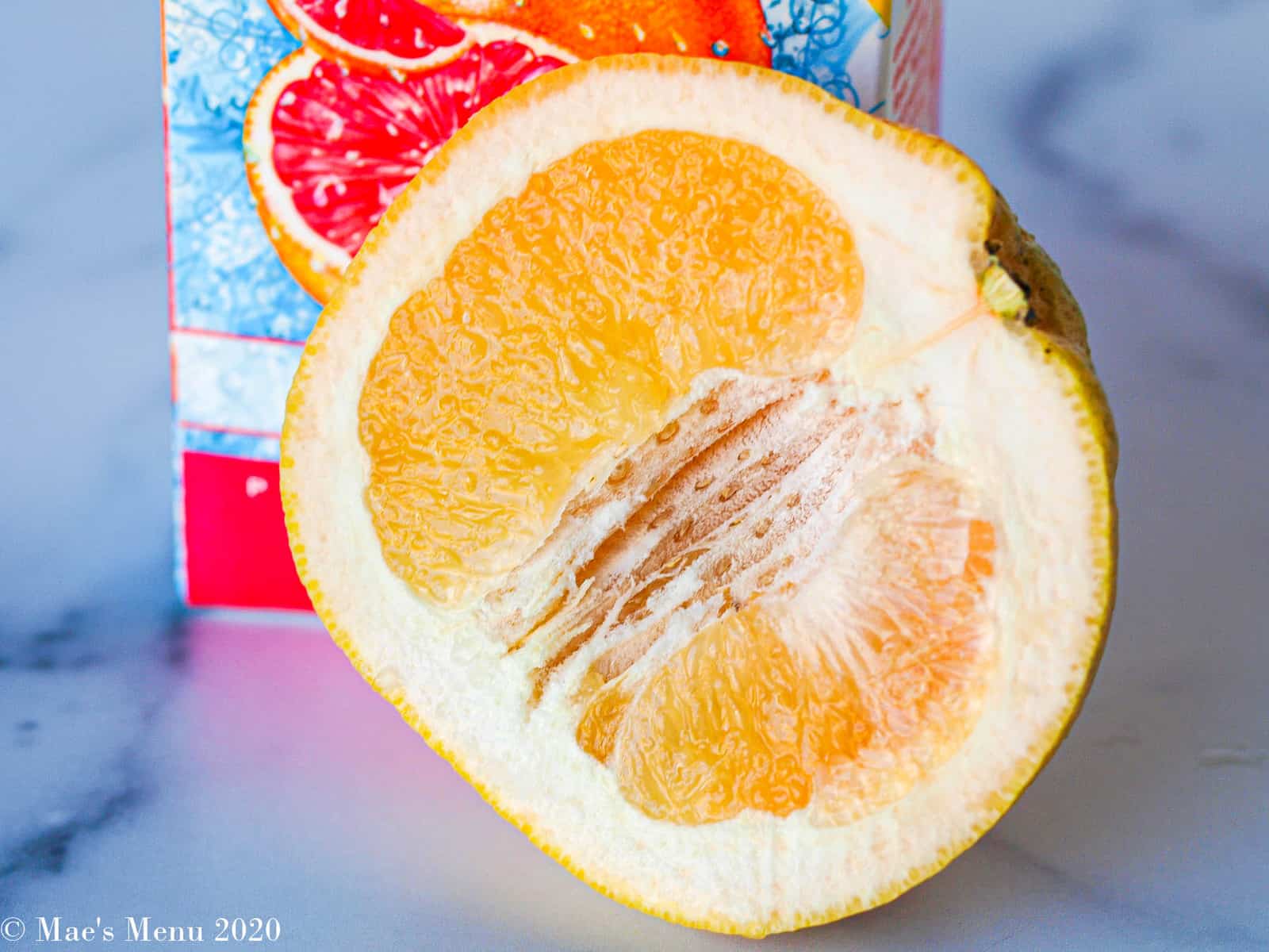 half a grapefruit sitting on its side in front of a carton of grapefruit juice