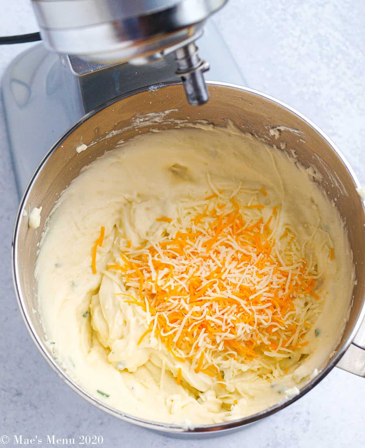 cheese on top of the creamy whipped potatoes in a stand mixing bowl