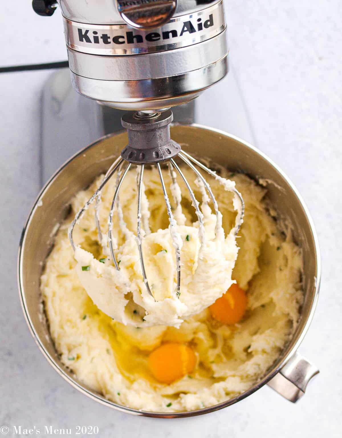 An overhead shot of a stand mixer with the mashed potatoes and eggs in it. 