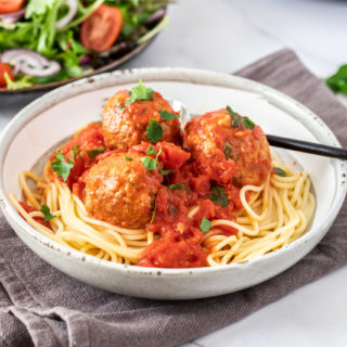 Healthy Turkey meatballs on a small bowl of pasta next to a small dish of salads