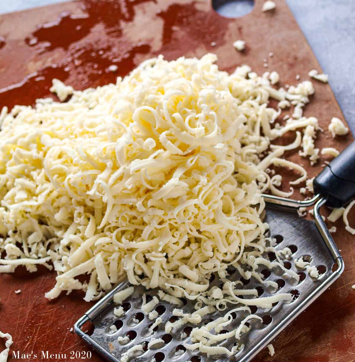 A wooden cutting board with shredded mozzarella cheese and a grater
