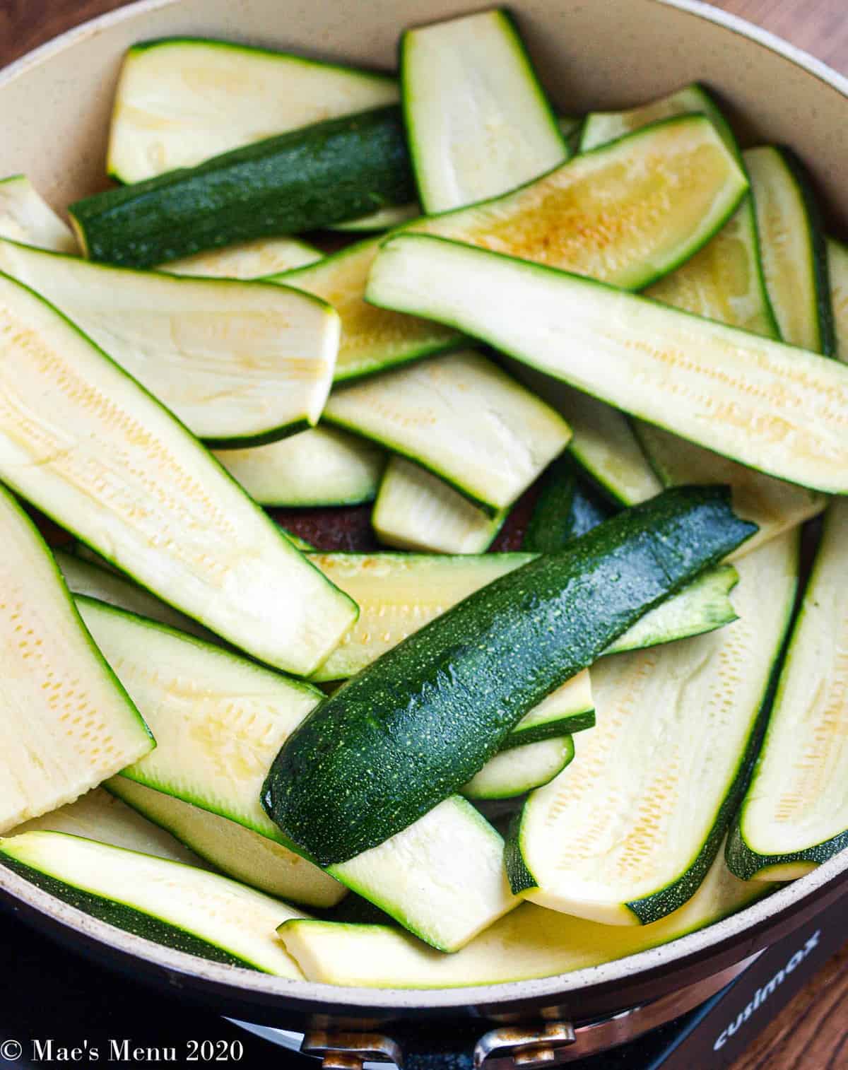 A saute pan full of zucchini slices cooking up
