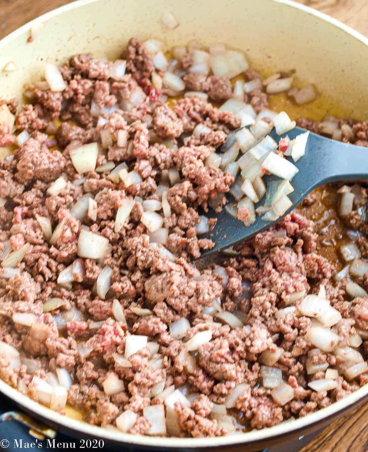 A side angle sot of a saute pan full of crumbled ground meat and onions