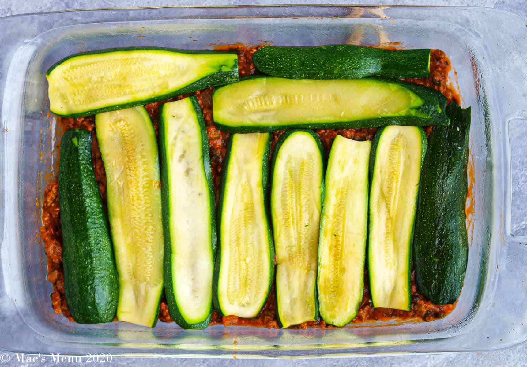 The first 2 layers of lasagna in a pan: meat sauce with zucchini slices on op