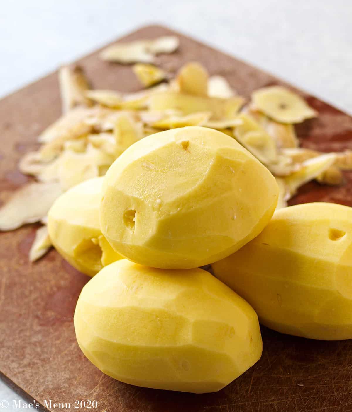 Peeled golden potatoes on a wooden cutting board with potato peels in the background