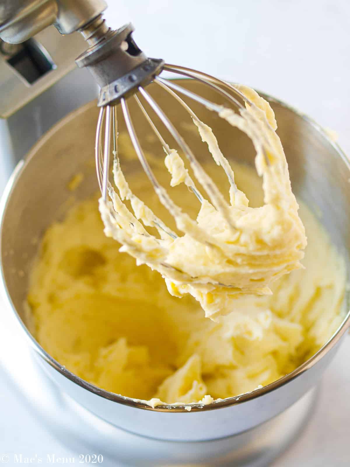A stand mixer whip attachment covered with whipped mashed potatoes