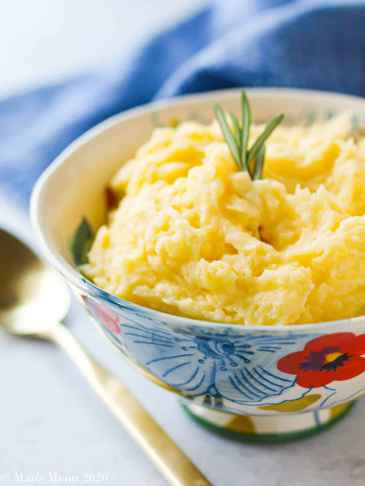 An up-close side angle shot of healthy mashed potatoes without butter with a gold spoon next to the floral bowl