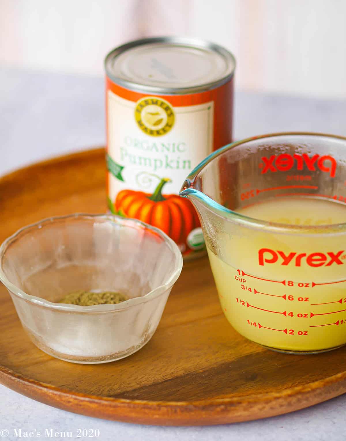 Some ingredients for parmesan pumpkin chicken: a can of pumpkin, a small dish of herbs and salt, and a measuring cup of chicken broth
