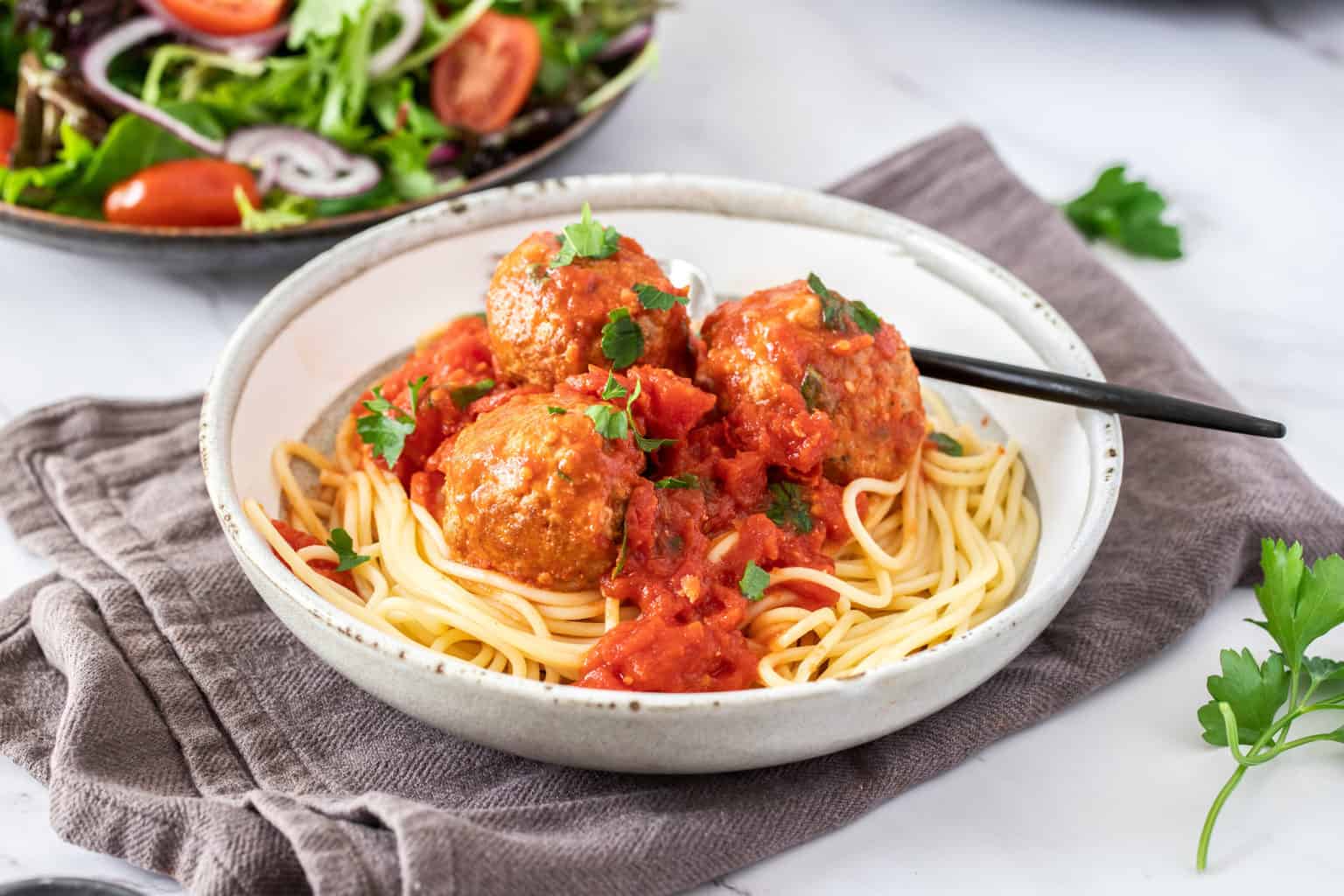 An up-close shot of a white bowl of spaghetti with healthy turkey meatballs on top