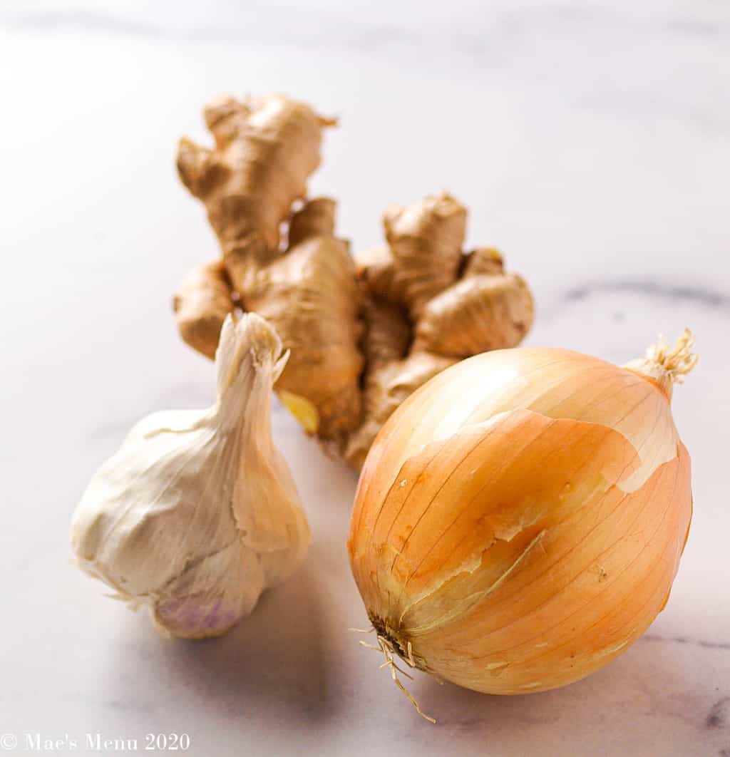 A photo of an onion, head of garlic, and large knob of ginger