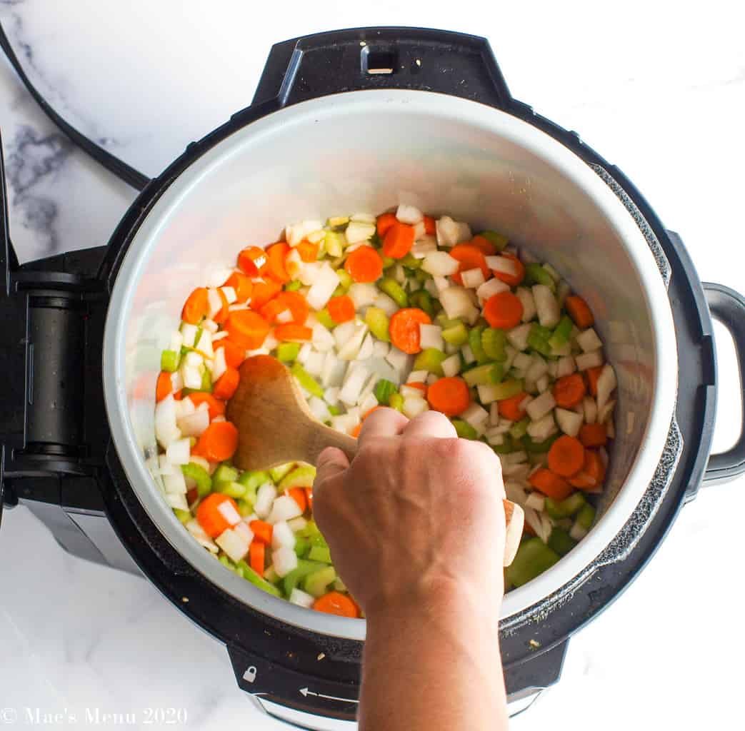 hand sauteing carrots, onions, and celery in a pressure cooker