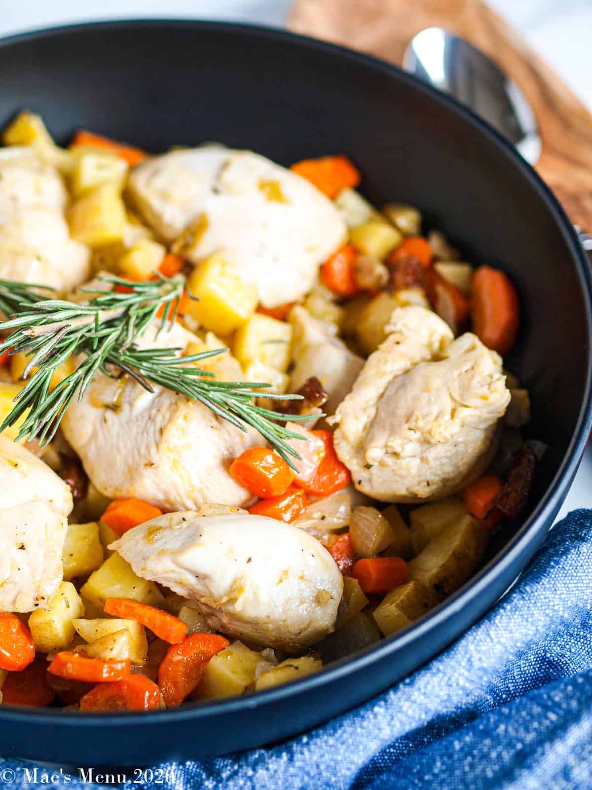 A side angle shot of a large black serving bowl of sheet pan apricot chicken with vegetables