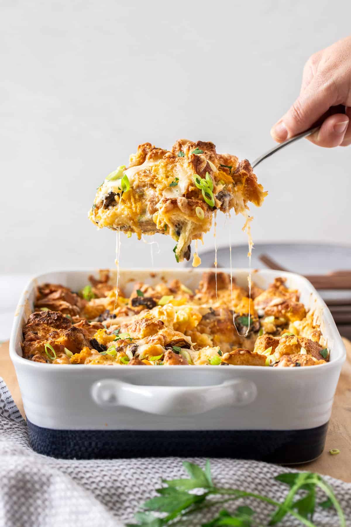 A large tray of savory bread pudding, taking a large scoop of the pudding out 