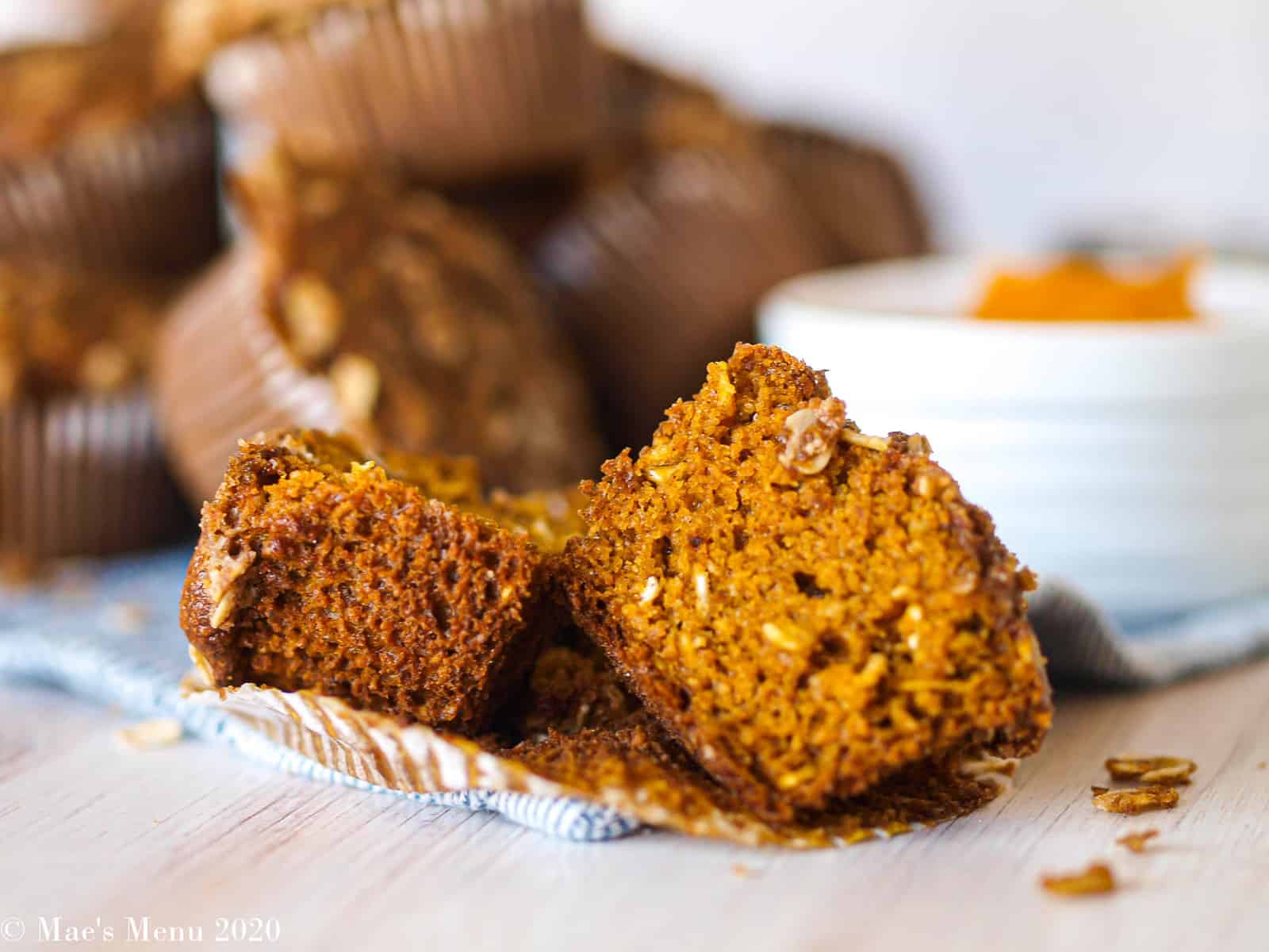 A split gluten-free pumpkin muffin in front of a stack of the muffins