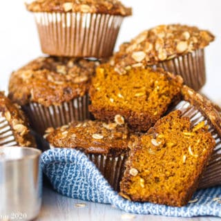 A pale of gluten-free pumpkin muffins on a blue towel with a silver measuring cup in front of them