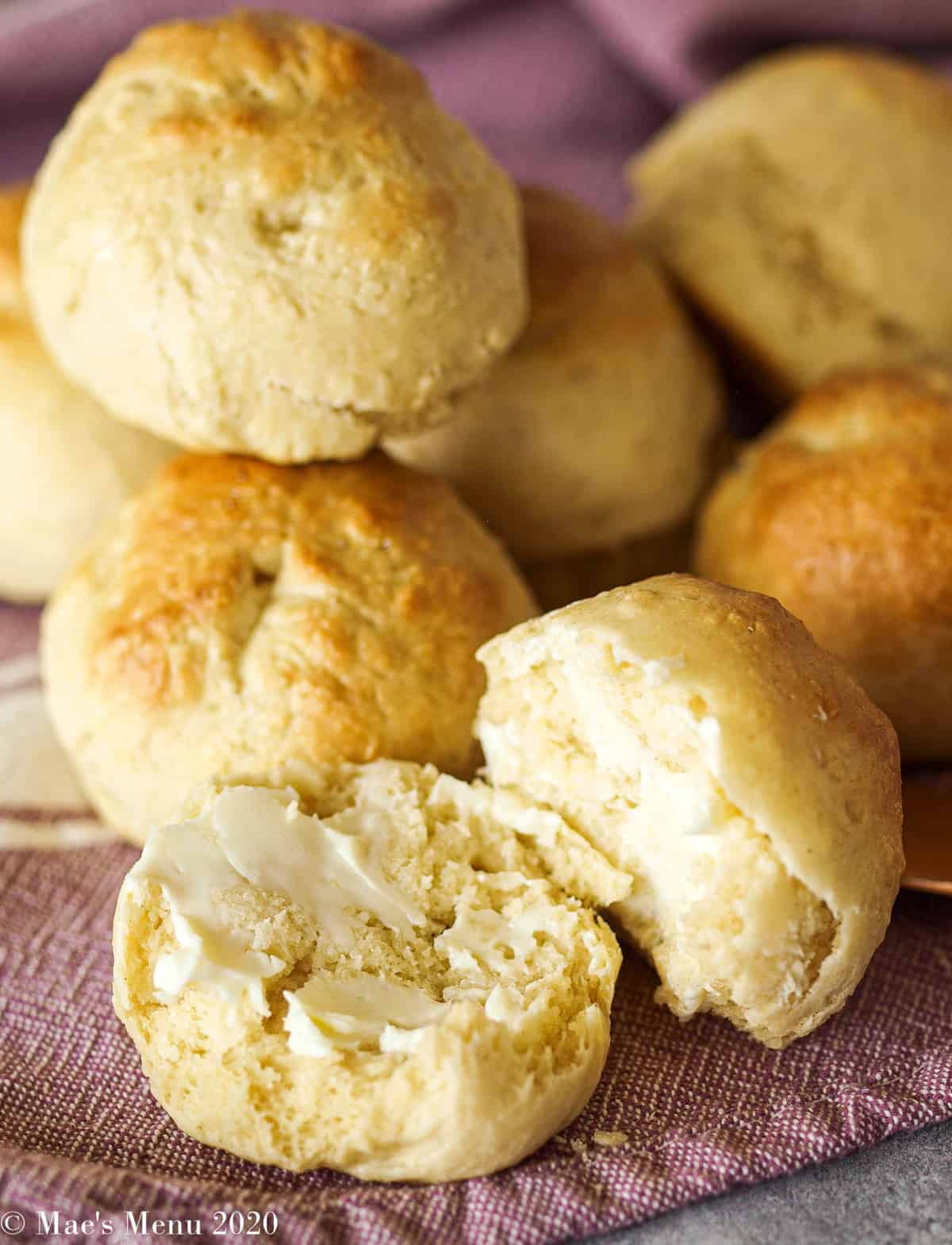 a pile of easy no-yeast dinner rolls. One roll in front is cut in half and brushed with butter
