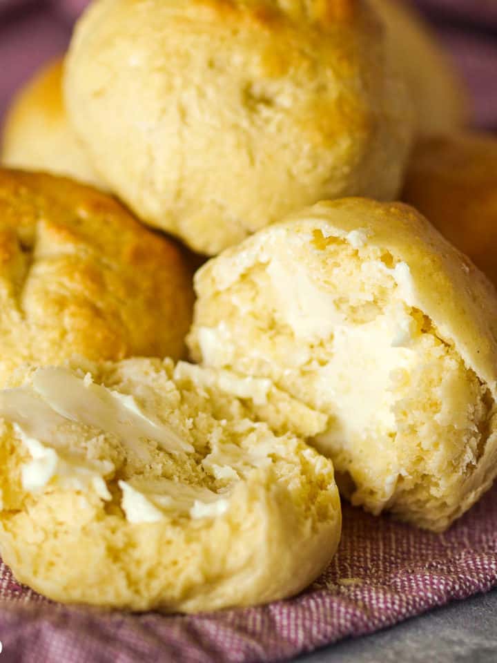 An up-close shot of a pile of easy no-yeast dinner rolls. One split in half with butter