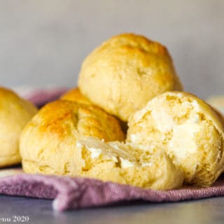 A stack of no yeast dinner rolls on a purple towel with a roll split in half with butter.