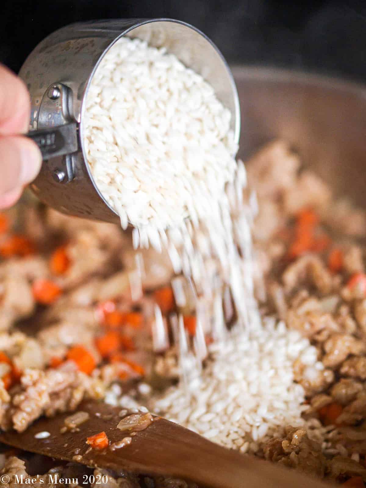 Pouring a cup of arborio rice into the saute pan