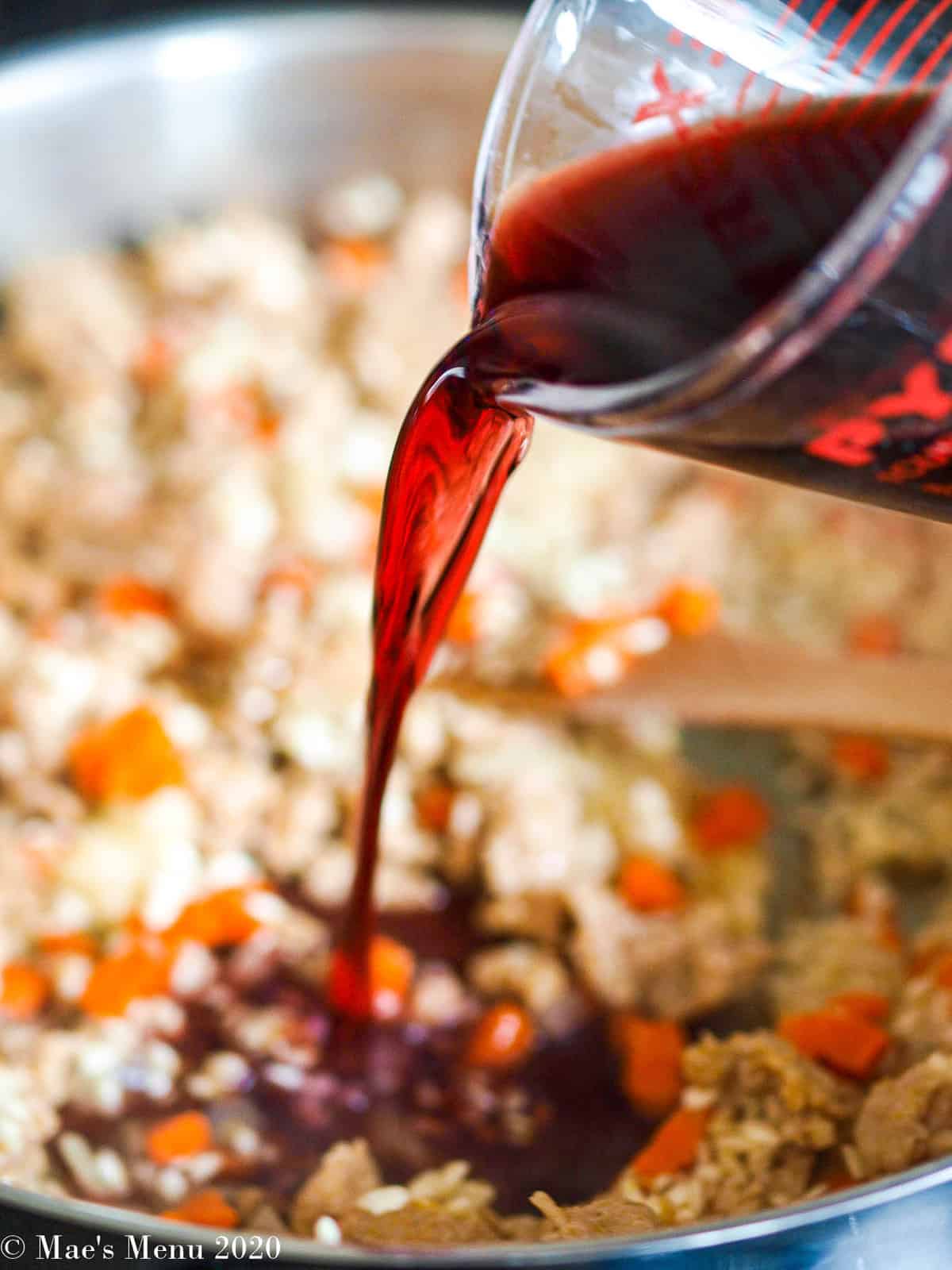 Pouring red wine into the pan of rice, meat, and vegetables