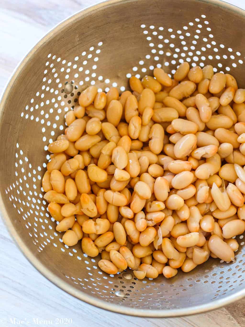 A metal strainer of white beans
