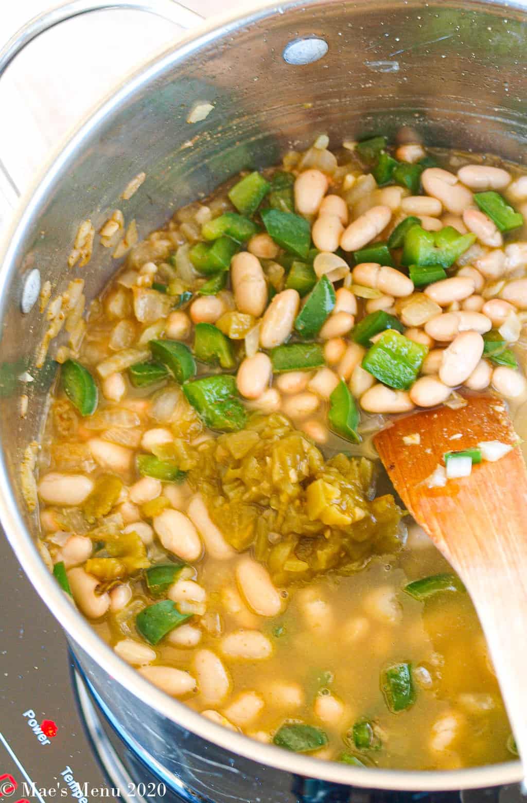 Beans, green pepper, white bean, green chiles, and chicken stock in a pot