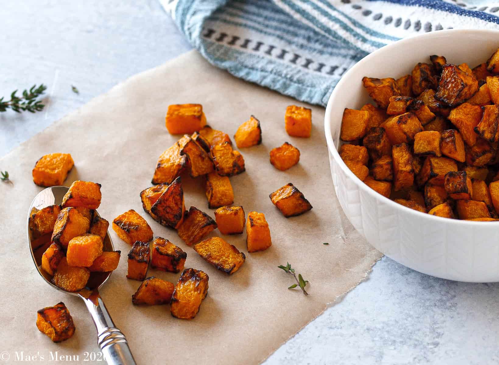 Air fryer butternut squash on a sheet of parchment paper with a spoon and in a white bowl