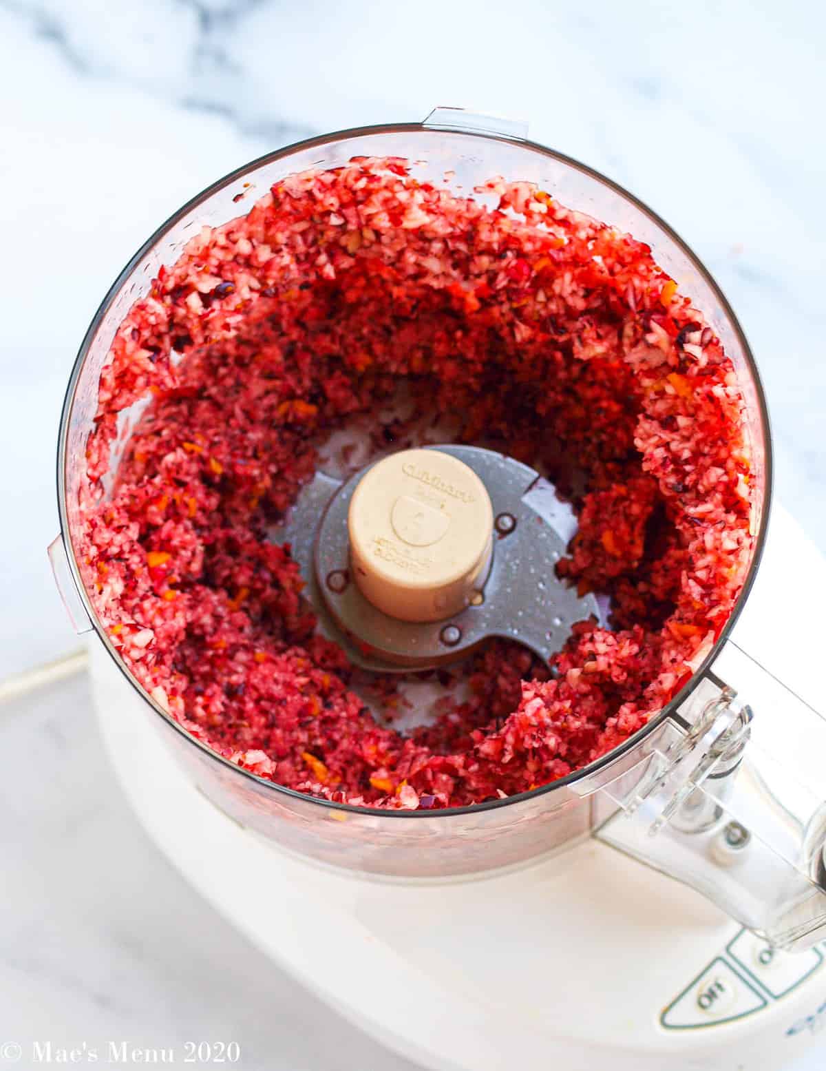 Pulsed cranberries, apples, and orange peel in the bowl of a food processor 