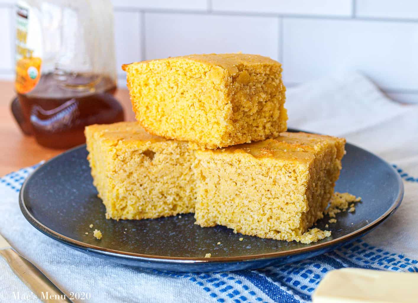 Three pieces of gluten-free cornbread on a blue plate with a bottle of honey in the background 