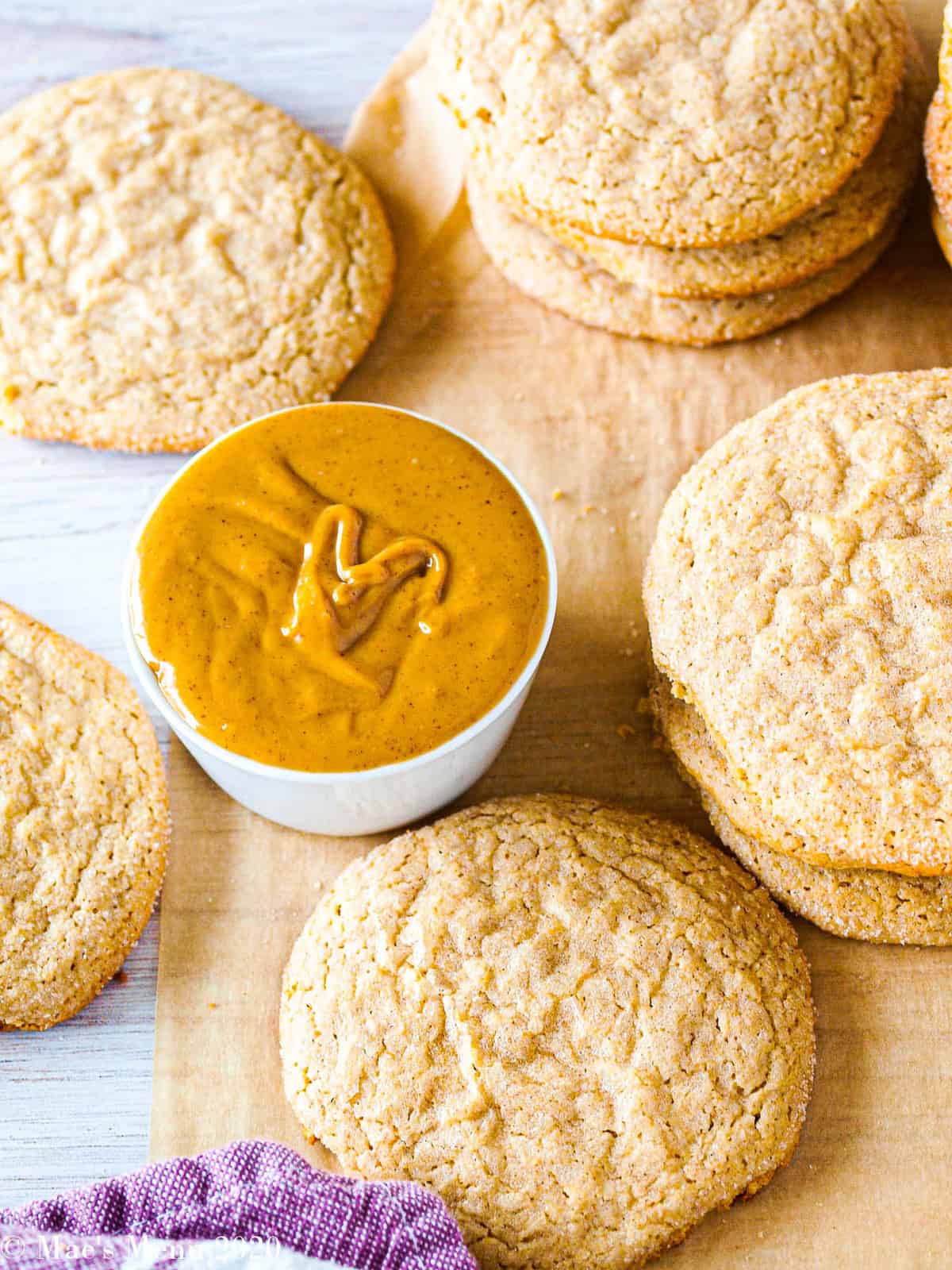 An overhead shot of stacks of peanut butter cookies surrounding a small cup of peanut butter 