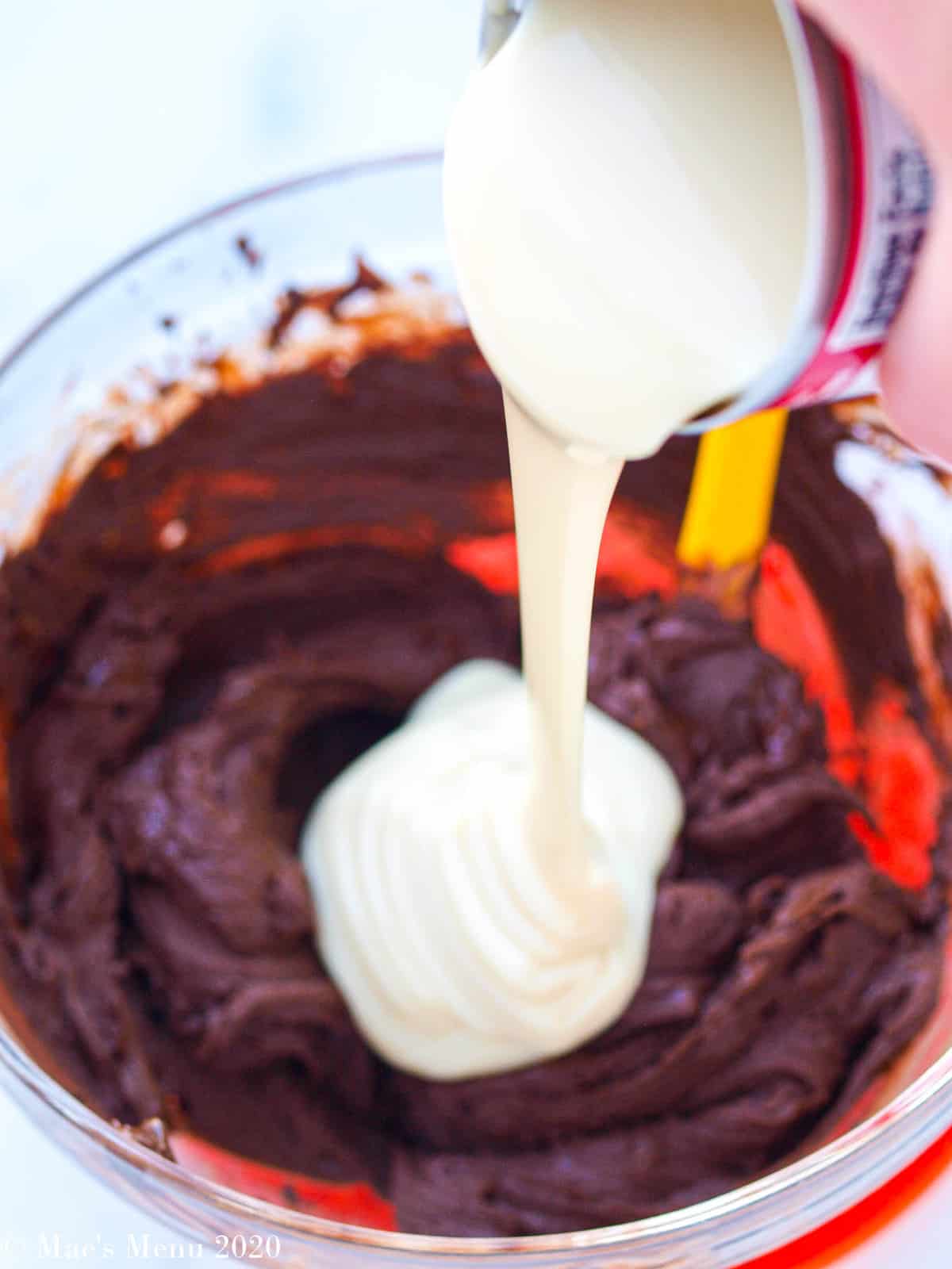 Pouring sweetened condensed milk into a bowl of melted chocolate