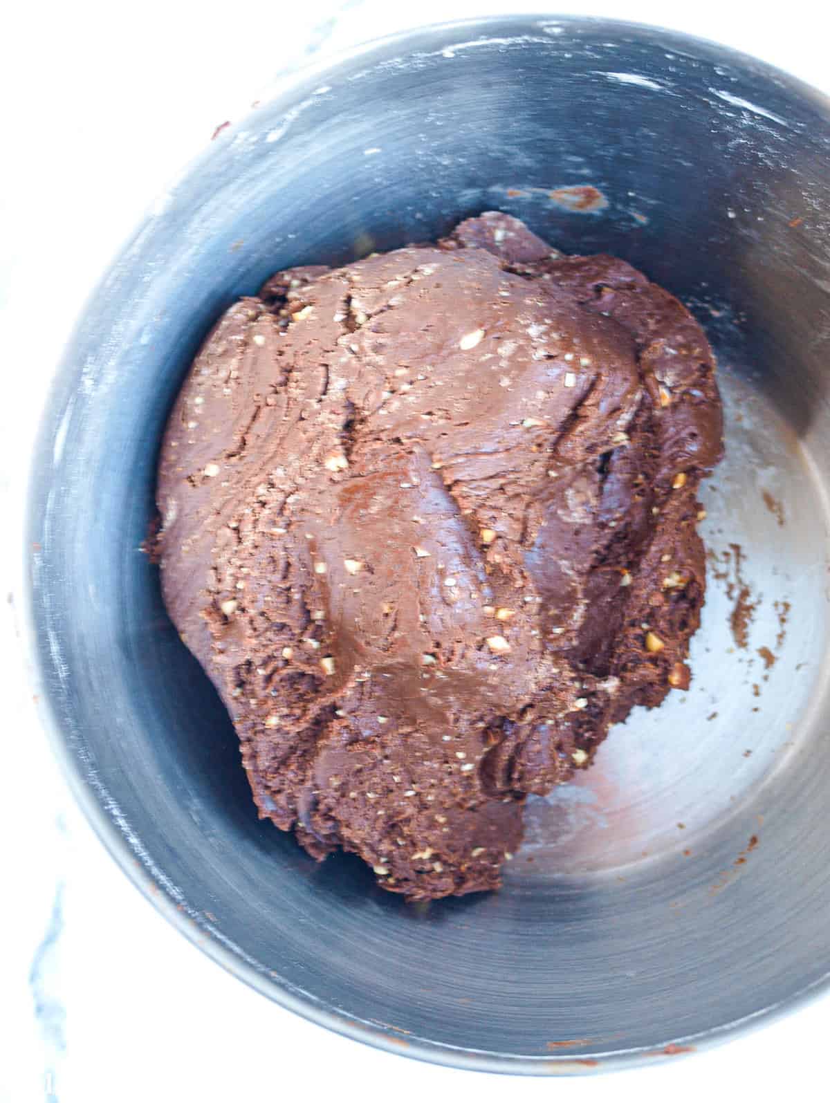 A large and thick chunk of fudgy bonbon batter in a large metal mixing bowl