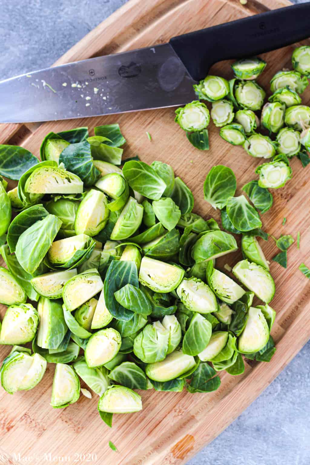 an overhead shot of a wooden cutting board of brussels sprouts with the ends trimmed off and the sprouts halved and quartered