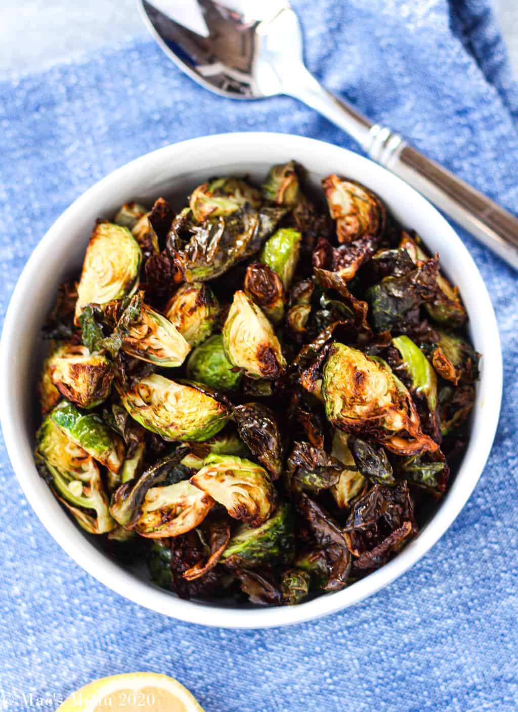 An overhead shot of a white bowl of air fryer brussels sprouts on a blue napkin