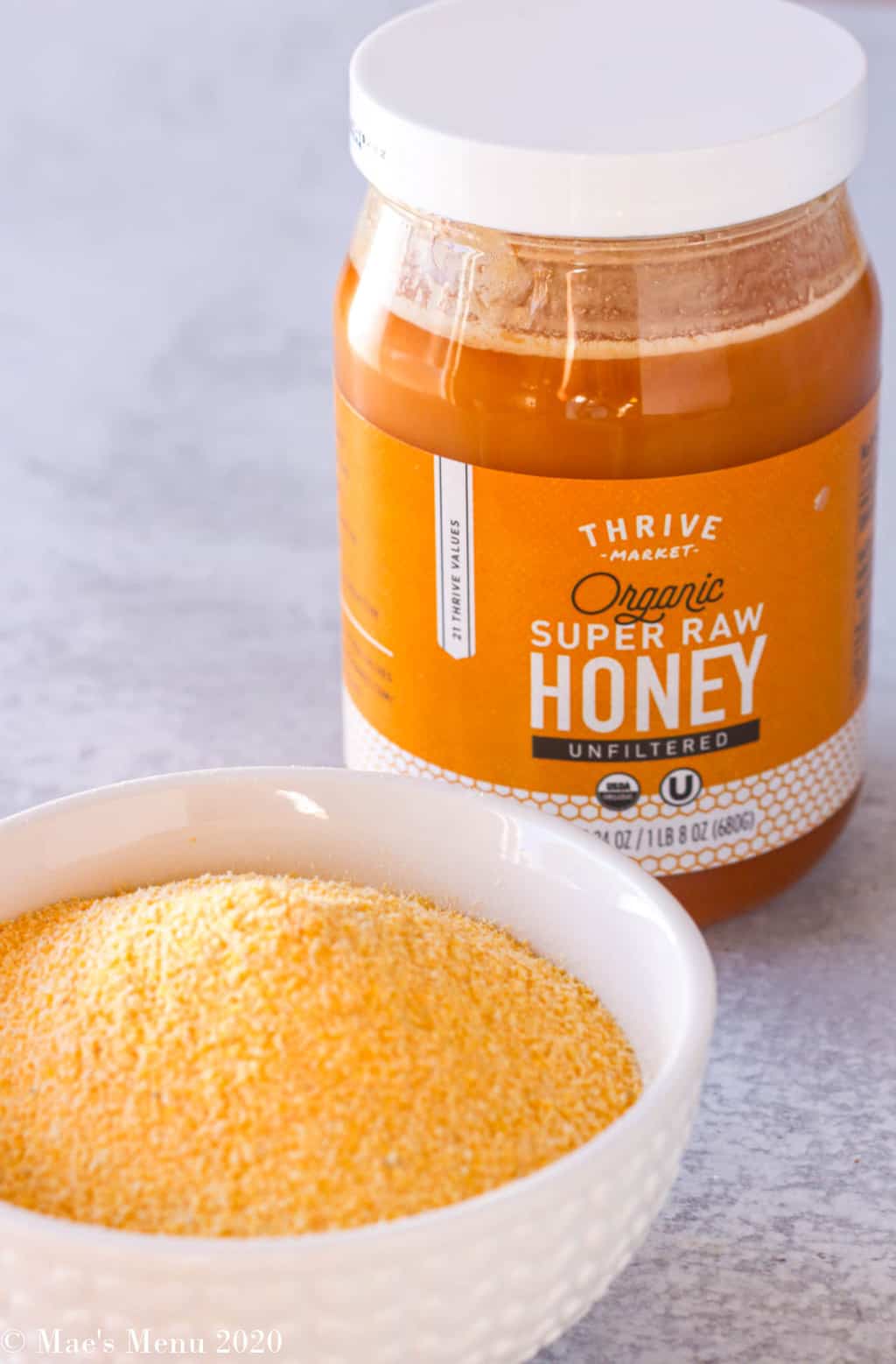 a jar of thrive market raw honey next to a small dish of yellow cornmeal