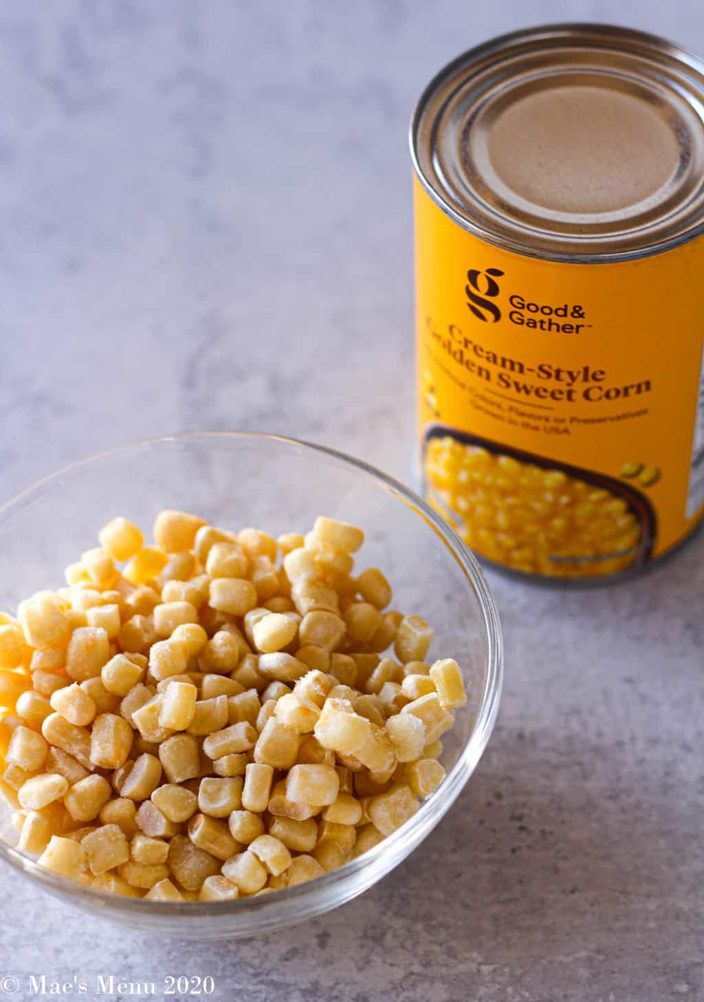 A can of creamed corn sitting by a glass bowl of corn