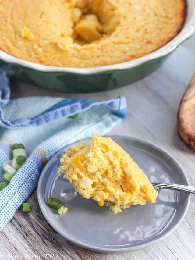 A scoop of corn casserole in front of a baking dish of it.