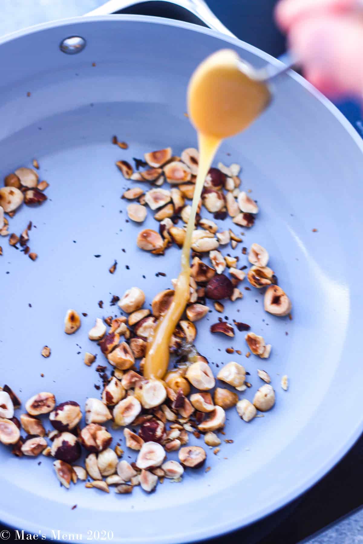 Drizzling honey over a pan of toasted hazelnuts