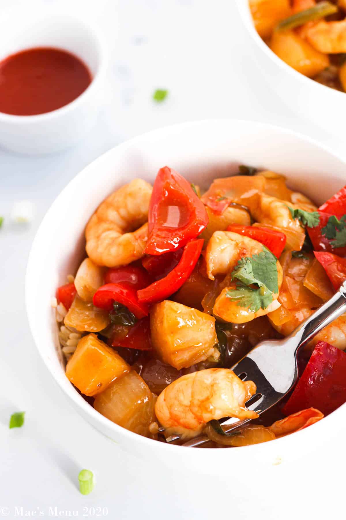 An angled up-close shot of sweet and sour shrimp with a fork in the bowl holding a shrimp