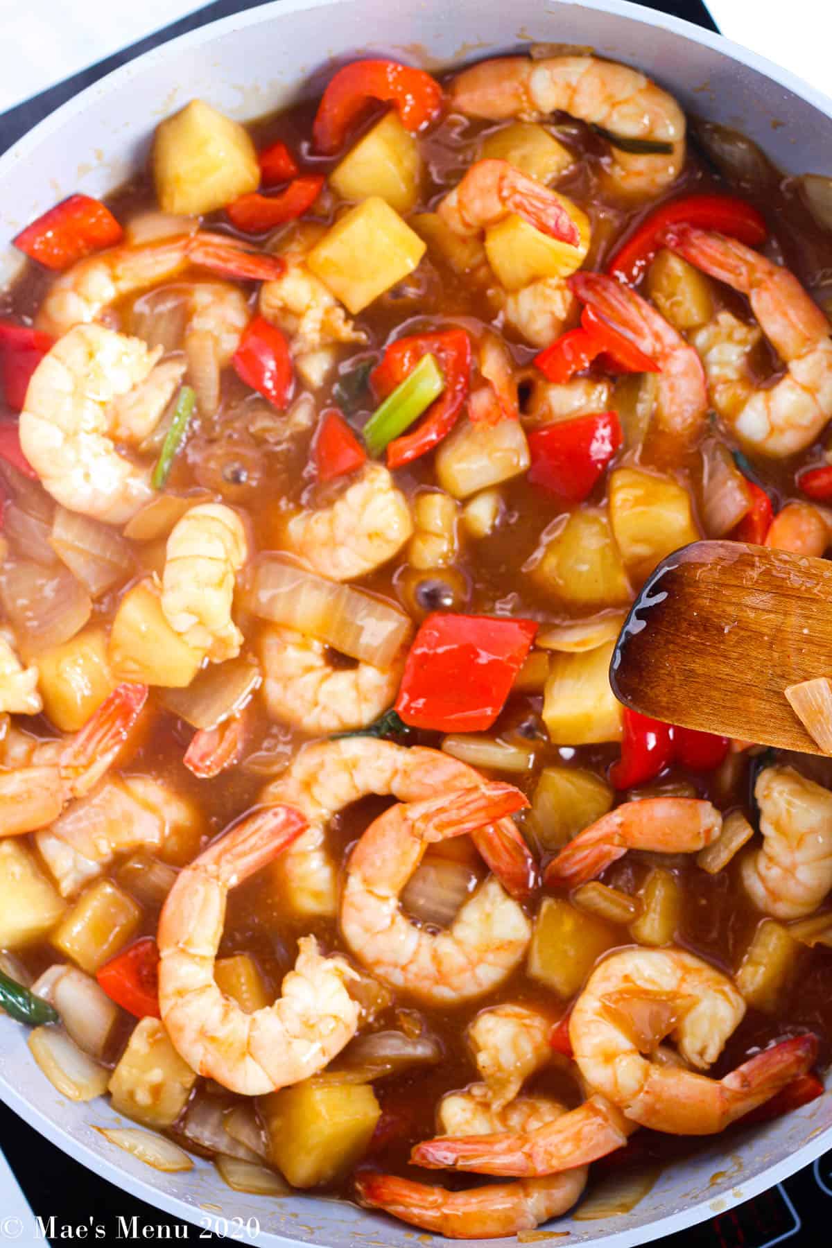 THe finished sweet and sour shrimp in a large nonstick pan with a wooden spoon on the side