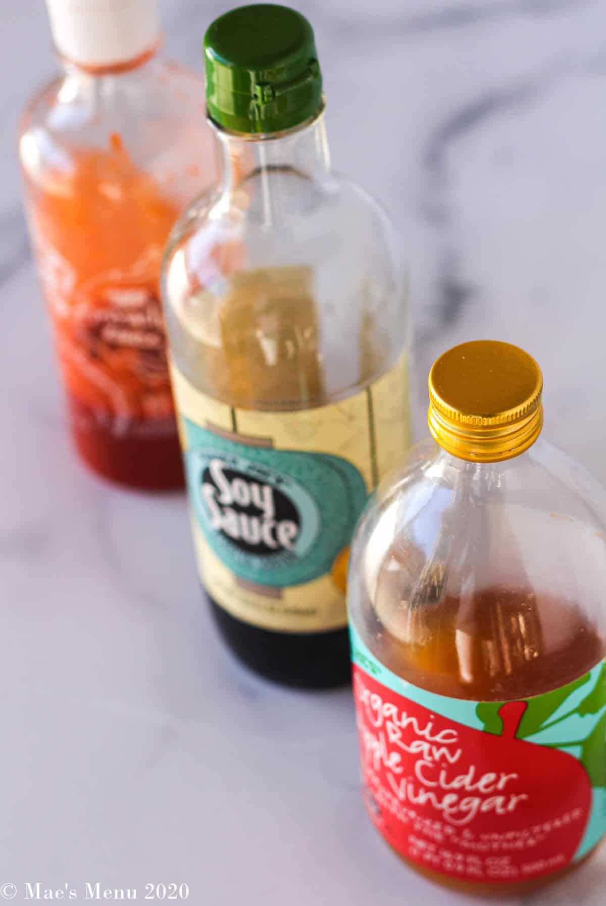 A bottle of apple cider vinegar, soy sauce, and sriracha on the counter