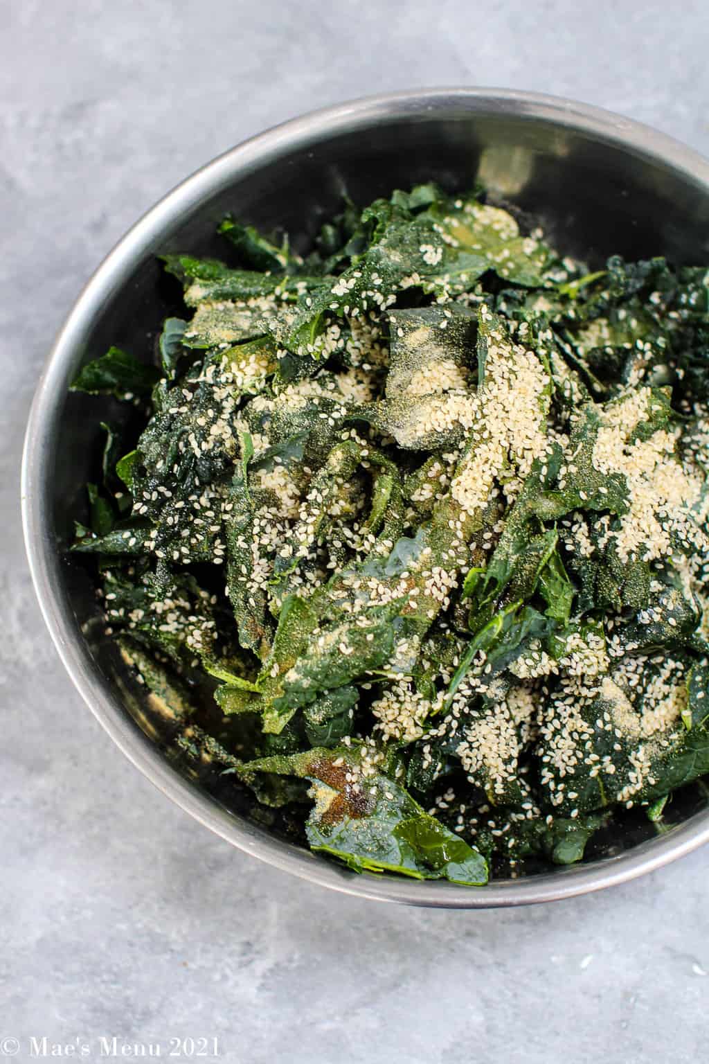 An overhead shot of kale in a bowl covere covered with liquid aminos, sesame seeds, and other seasonings