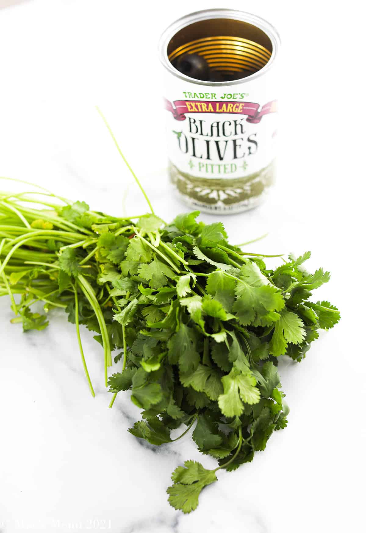 A bunch of cilantro next to an open  can of black olives 