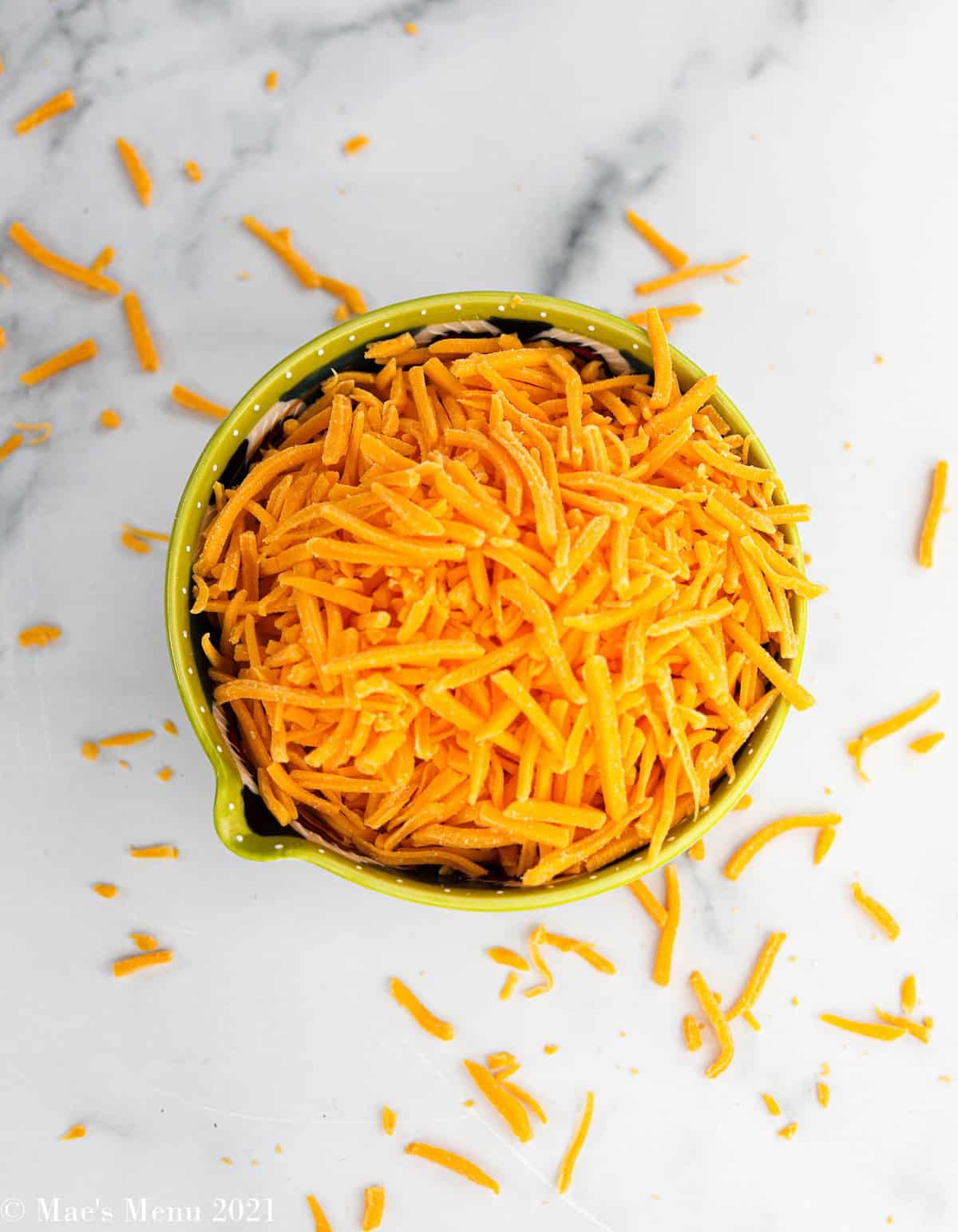 An overhead shot of a small dish of shredded cheddar cheese