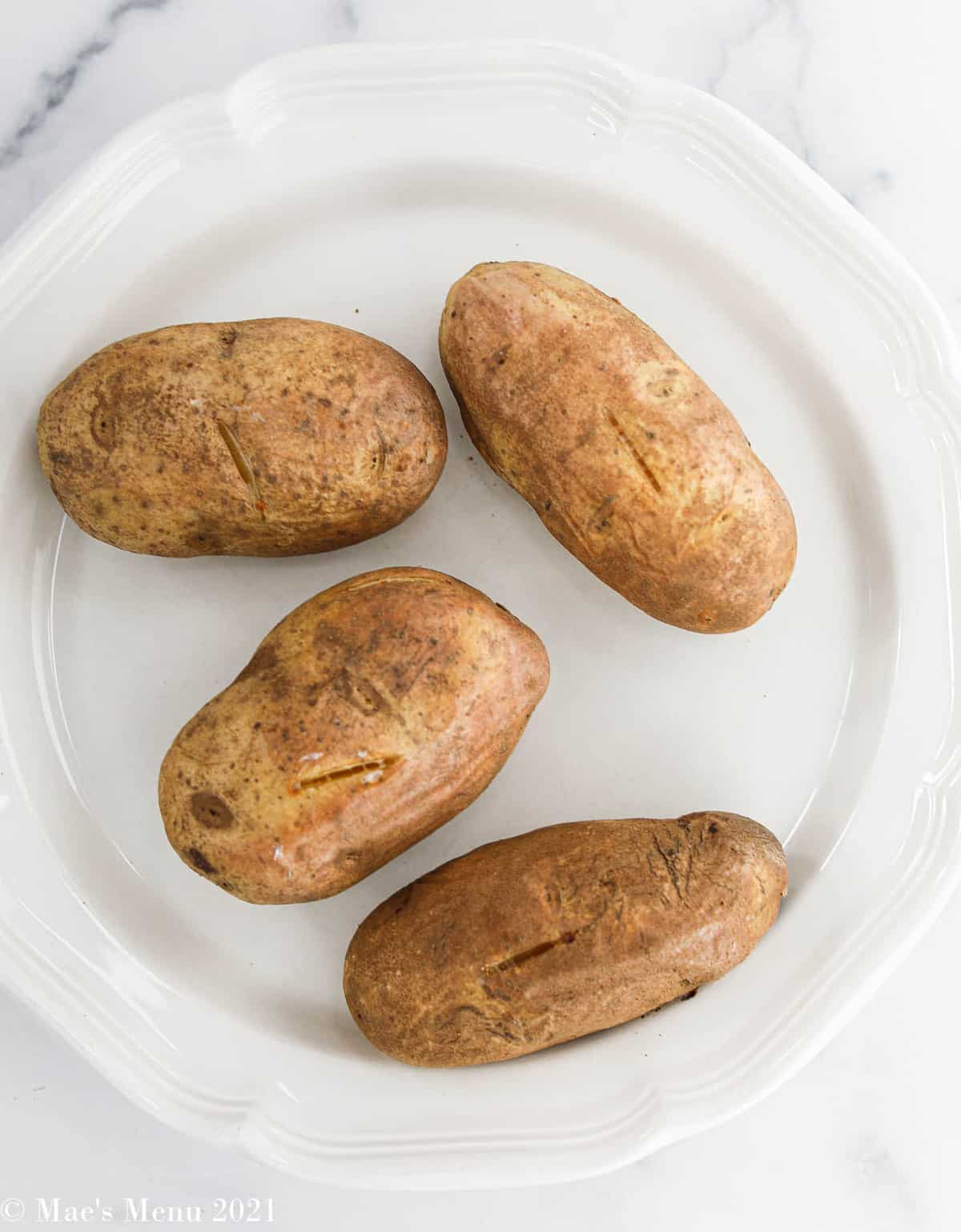 4 baked russet potatoes on a white plate