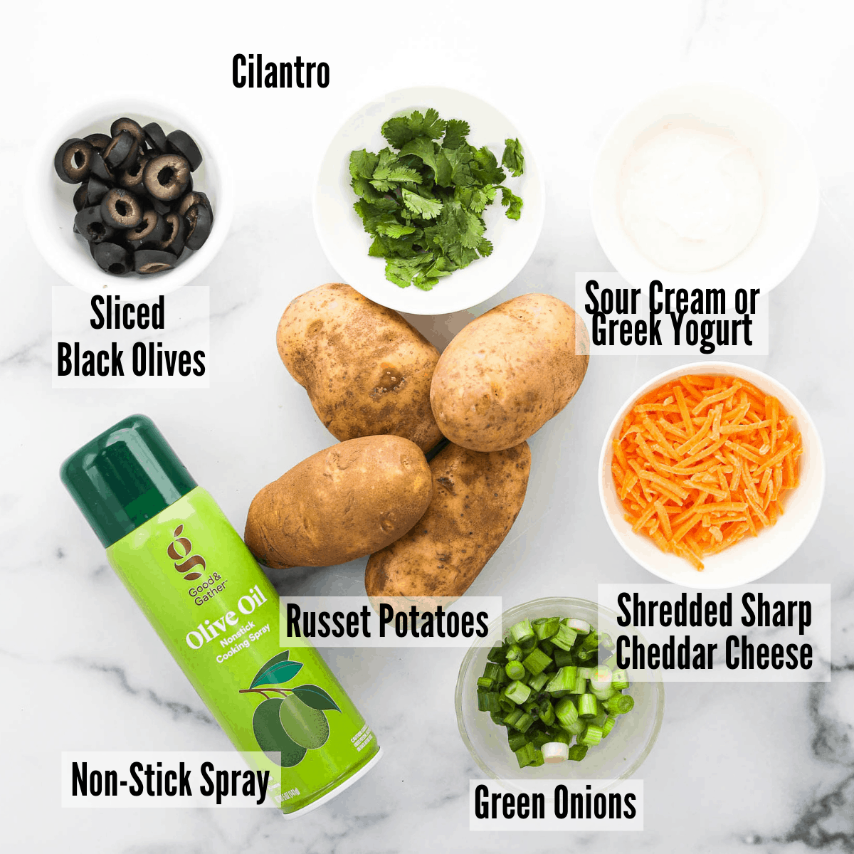 All of the ingredients for air fryer potato skins: russet potatoes, sliced black olives, cilantro, sour cream and greek yogurt, shredded sharp cheddar cheese, non-stick spray, and green onions