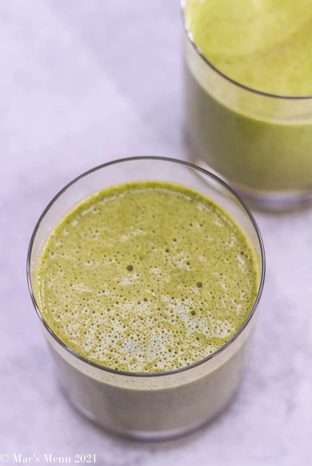 An up-close overhead shot of a green peanut butter date smoothie in a small clear glass 