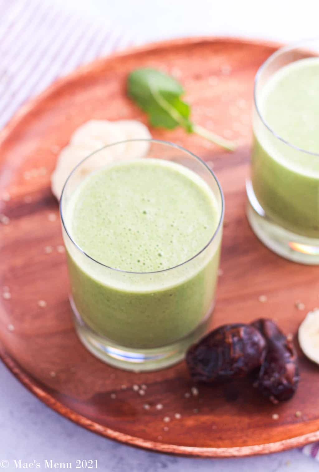 An up-close overhead shot of a cup of green date smoothies on a wooden cutting board